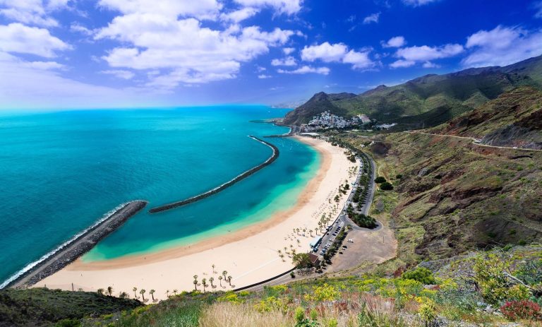 Blick auf die Küste mit Sandstrand, klarem Wasser und Bergen auf Teneriffa.