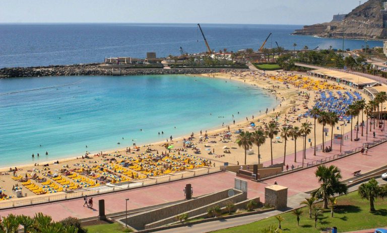 Blick auf einen Strand mit gelben Liegen, Sonnenschirmen und klarem Wasser auf Gran Canaria.